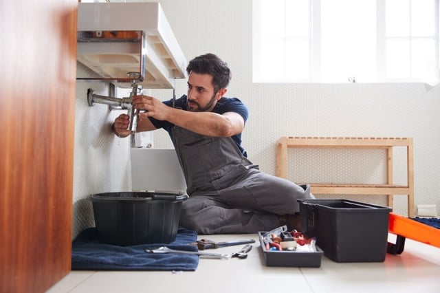 plumber fixing leaking pipes in bathroom